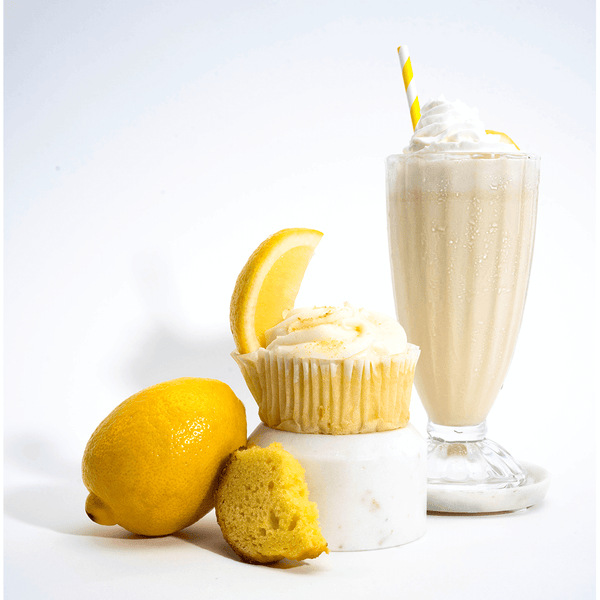 A glass of lemon cake shake next to a lemon cake and a fresh lemon.
