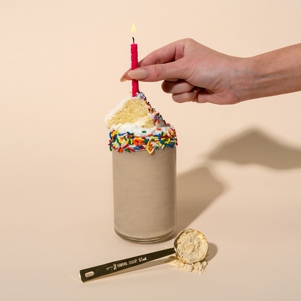 Birthday cake protein shake topped with whipped cream, sprinkles and a lit candle