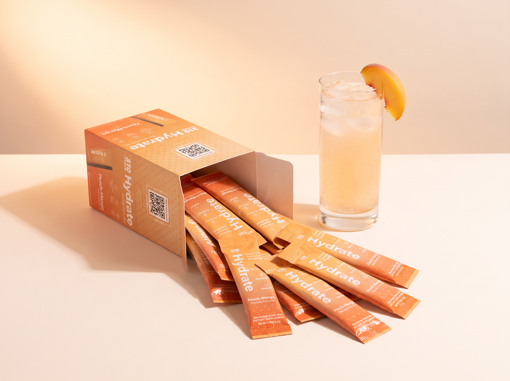 310 Hydrate Peach Mango 15-count box with sticks and a peach glass on a warm cream backdrop