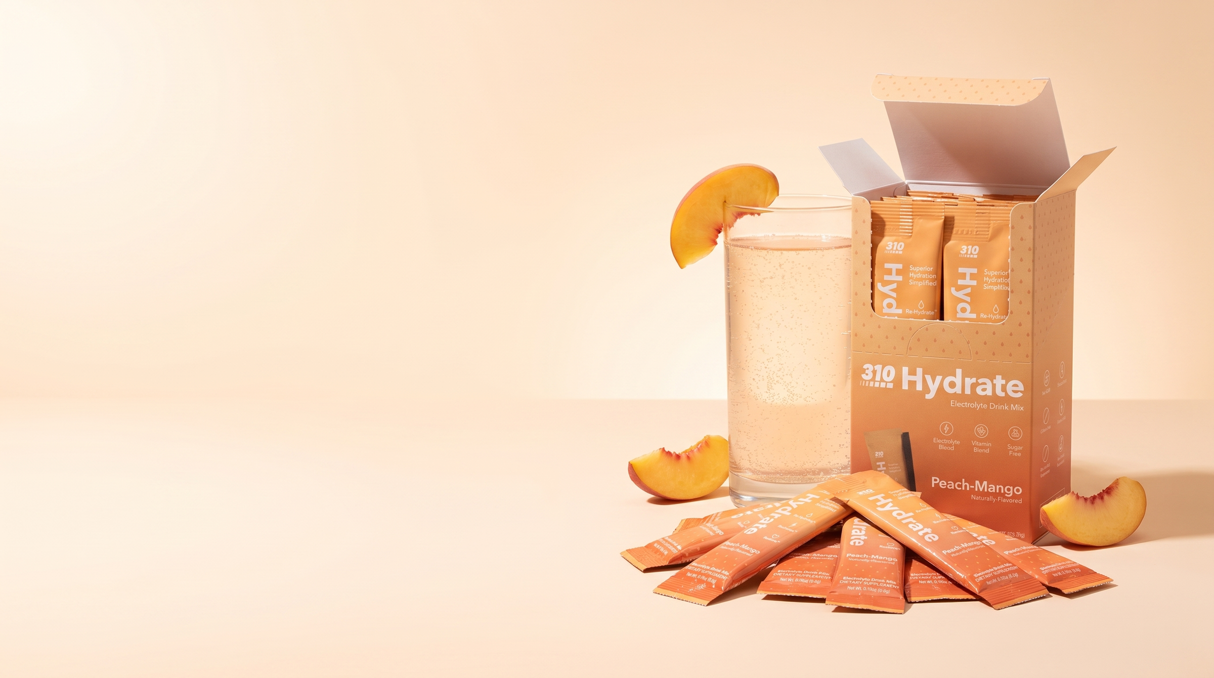 310 Hydrate Peach Mango 15-count box with sticks and a peach glass on a warm cream backdrop