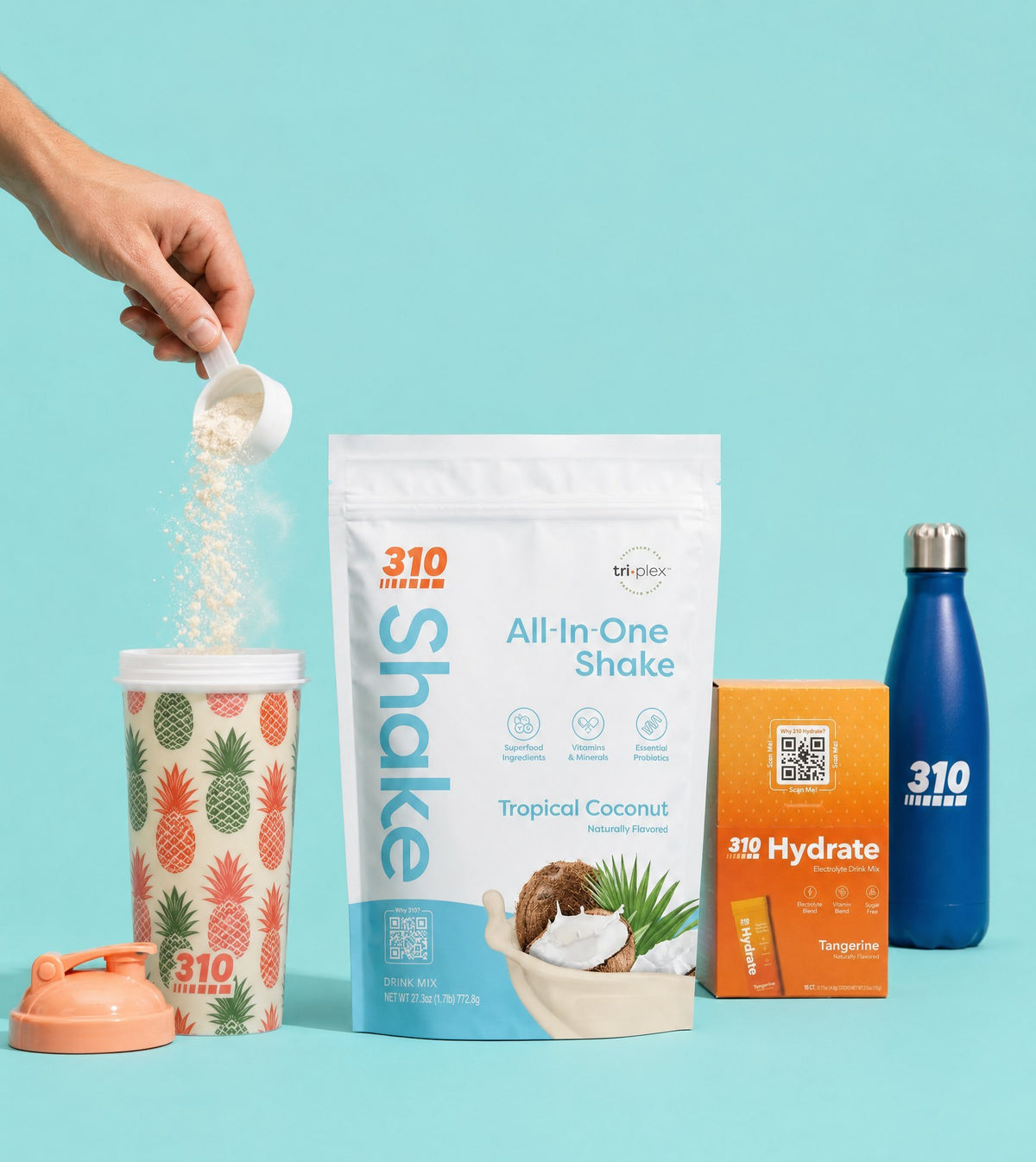A scoop of 310 Tropical Coconut shake poured into the pineapple shaker, with the Tropical Coconut pouch, Hydrate Tangerine box and navy 310 bottle