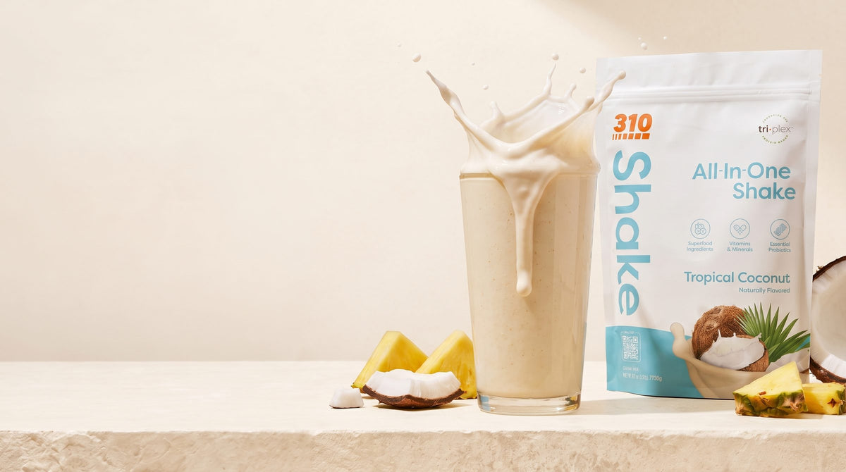 Tropical Coconut shake with a milk splash beside the 310 Tropical Coconut pouch on a cream ledge