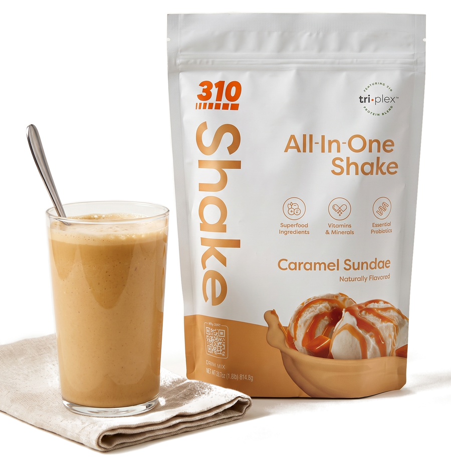 A creamy 310 Caramel Sundae shake in a glass with a spoon, next to the Caramel Sundae All-In-One Shake pouch