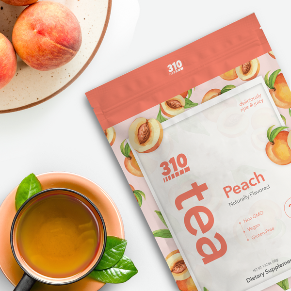 A flat lay photo of 310 Peach tea with a cup of tea and peaches on a white surface
