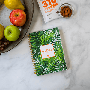 90-day wellness journal, a bowl of fresh fruits, almonds and chocolate meal replacement