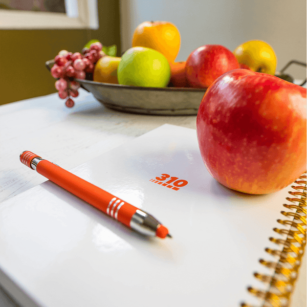 wellness journal, an orange pen and an apple