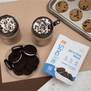 A flat lay of 310 cookies n' cream pouch with two glasses of shake, cookies and a bowl of biscuit.