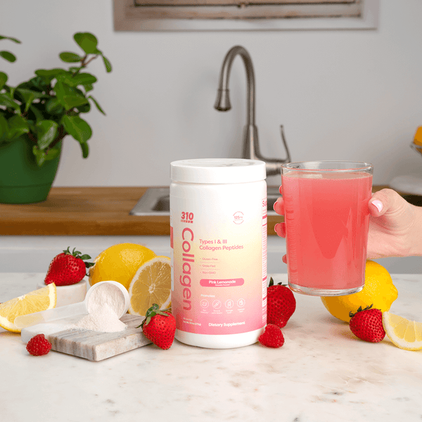 310 Collagen Pink Lemonade and a hand holding a glass of collagen in a kitchen counter top