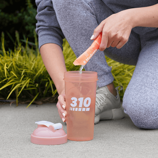 woman pouring peach-mango hydrate into the shaker cup